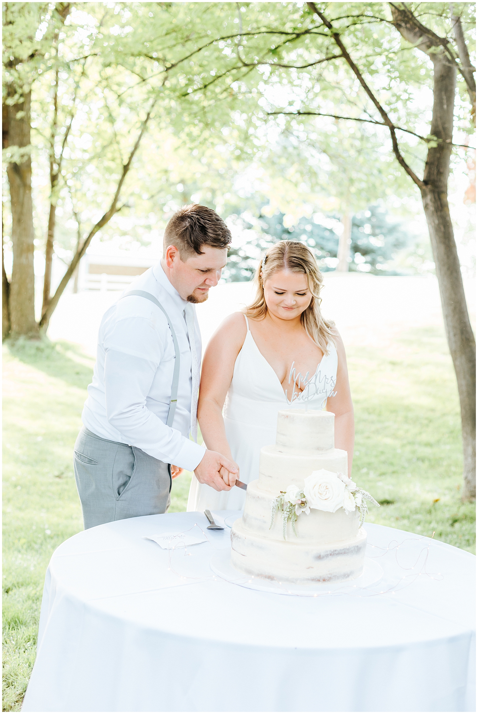 Bride and Groom cutting their cake - tiered white naked wedding cake with simple flowers