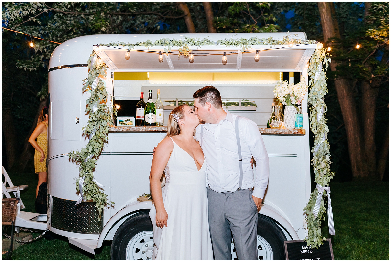 Bride and Groom Kiss in front of Whimsical Wagons horse trailer mobile bar