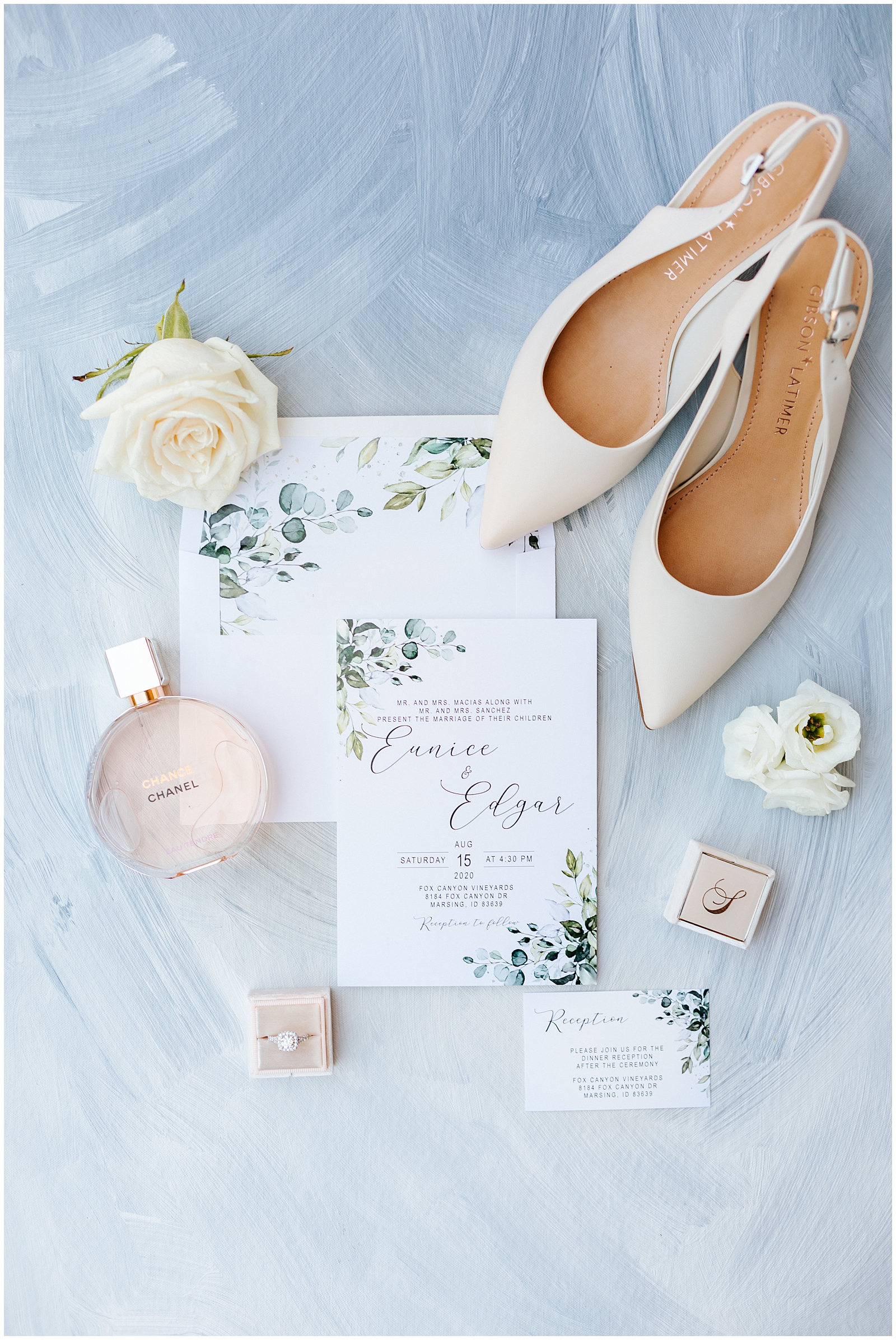 Wedding Details Flatlay against Dusty Blue background with fresh Florals, nude heels, chanel perfume, and Mrs. Box ring Box