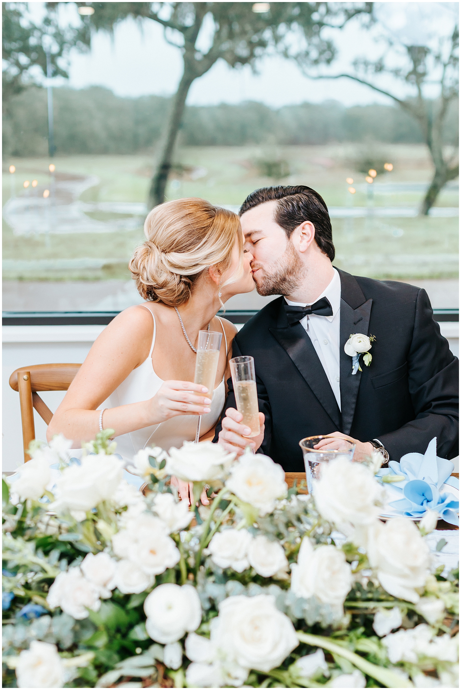 Bride and Groom Kissing with a Champagne Toast at Sweetheart Table at Simpson Lakes Wedding 
